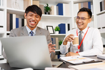 Two men are sitting at a desk, one of them is holding a piece of paper. They are having a conversation, and it seems like they are discussing something important. The atmosphere is tense
