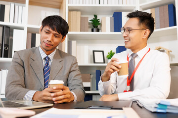 Two men are sitting at a desk, one of them is holding a piece of paper. They are having a conversation, and it seems like they are discussing something important. The atmosphere is tense
