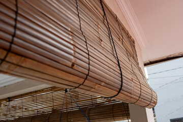 Close‑up of rolled bamboo blinds hanging on a modern house facade, showing natural wood texture, eco friendly sun shade design, and tropical exterior decor detail.