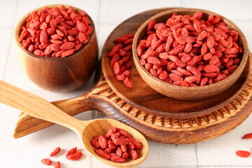Wooden bowls and spoon with dried goji berries on white tile background, closeup