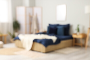 Blurred view of stylish bedroom with navy blue linen, tables and folding screen