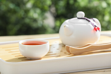 Tray with teapot and cup of tea on wooden table outdoors