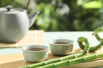 Board with cups of tea and bamboo stems on wooden table outdoors