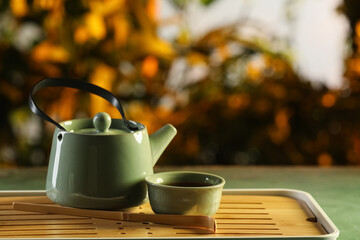 Tray with teapot and cup of hot tea on green grunge table outdoors