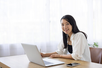 Smiling Woman Taking Notes While Working on Laptop at Desk