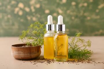 Bottles of dill seed essential oil on beige table against green background