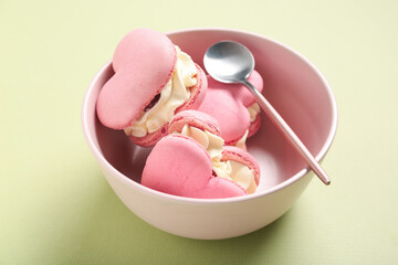 Bowl with sweet heart-shaped macaroons on green background. Valentine's Day celebration