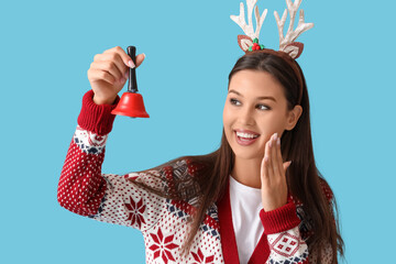 Beautiful young woman in pajamas and reindeer horns with jingle bell on blue background. Christmas celebration