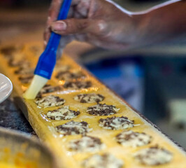 Close-up of a cook brushing egg wash on handmade ravioli dough filled with minced meat in a professional kitchen. Shows the authentic step-by-step cooking process, food craftsmanship, and traditional 