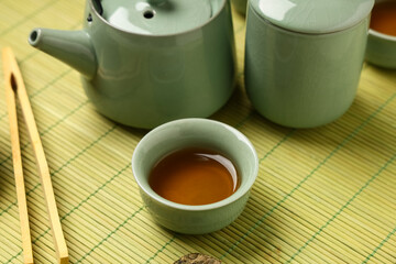 Teapot with cup of tea and tongs on green bamboo mat