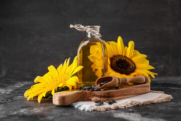 Wooden cutting board, bottle of sunflower oil and scoop of seeds on black grunge background, closeup