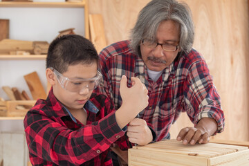 LClose up lovely Asian carpenter boy practice skill of screw knot on woodworking table carpentry shop with copy space, adorable boy with plaid shirt smiling hold carpenter tools in workshop at home