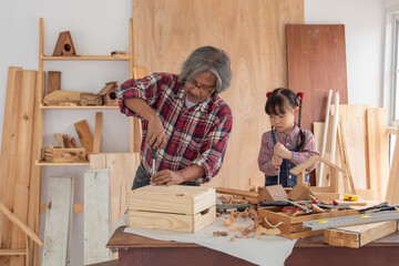 Asia retirement carpenter man spends time with cheerful granddaughter in carpentry studio, aged people enjoy teaching woodwork skill to adorable niece, family hobby lifestyle parenthood DIY handmade