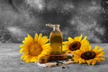 Wooden cutting board, bottle of sunflower oil and seeds on grey grunge background, closeup