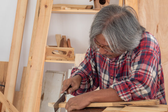 Elderly lifestyle working after retirement concept, healthy senior carpenter happy working in carpentry home studio, aged man with silver hair create his DIY handmade using a chainsaw to cut woodwork - Powered by Adobe