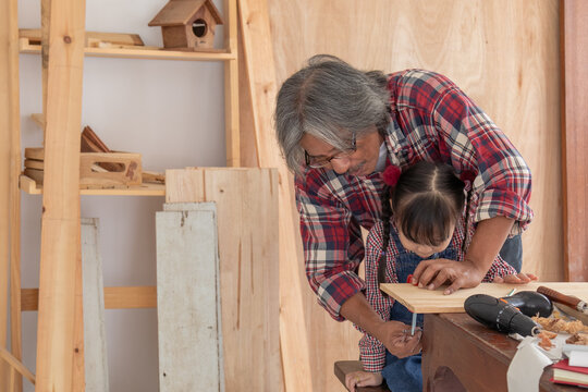 Elderly lifestyle working after retirement concept, healthy senior carpenter happy working in carpentry home studio, aged man with silver hair create his DIY handmade using a chainsaw to cut woodwork