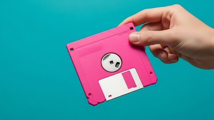 Concept of outdated technology and data archiving, a person's hand presenting a bright pink vintage floppy diskette on a blue studio background