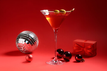 Glass of tasty red martini, disco ball, gift box and Christmas balls on red background