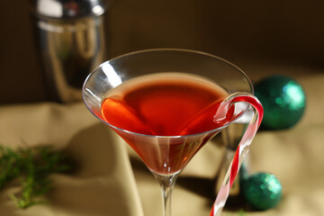 Glass of tasty red martini with candy cane on beige fabric as background, closeup
