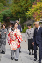 Obraz premium A woman wearing a red kimono is walking down a sidewalk with a baby in her arms. She is surrounded by other people, some of whom are also wearing kimonos. The scene is lively and bustling