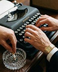 Woman typing on vintage typewriter and putting out cigarette.