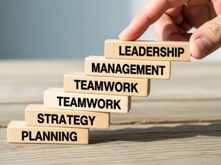 Hand placing leadership block atop management teamwork strategy planning blocks on wood surface