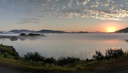 Fototapeta premium Sunrise over a misty lake with islands and distant mountains.