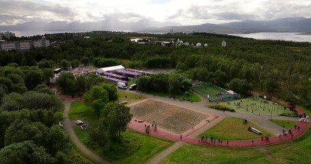 Aerial view of cancer Life race charity relay event with crowds walking and running around a track in Tromsø, Norway, surrounded by trees, sports facilities and dramatic Arctic scenery