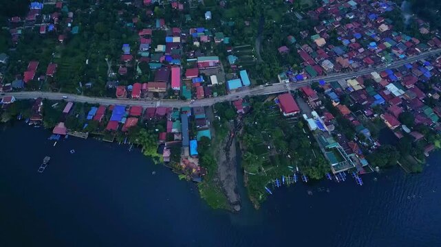 A tilt-down aerial of Talisay town revealing colorful rooftops and shoreline curves beside Taal Lake in Batangas, Philippines
