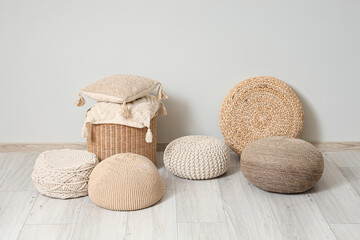 Different stylish poufs and wicker table with soft pillows near grey wall in room