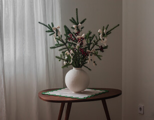 Spruce branches decorated with bows - a christmas bouquet in a ceramic vase on a wooden table