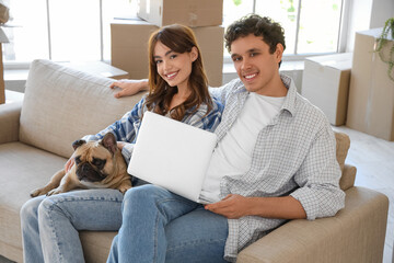 Young couple with French bulldog and laptop sitting in rented apartment on moving day