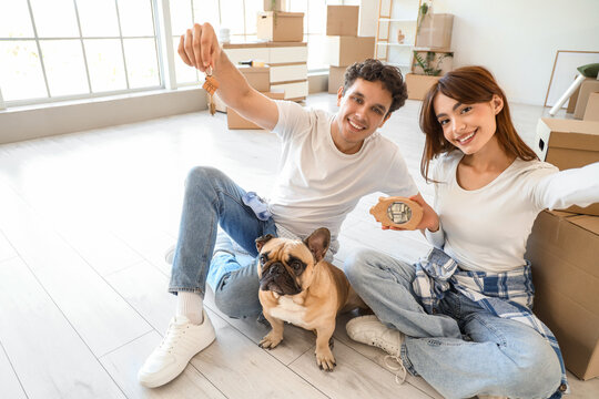 Young couple with French bulldog and piggy bank taking selfie in rented apartment on moving day