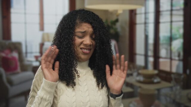 African american woman wearing cable knit sweater cringes and pulls back with raised hands in building interior; disgust.