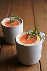 Grapefruit and rosemary infused beverage in white mugs on a wooden surface top view