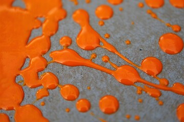 Orange paint splatters on a gray surface creating an abstract and vibrant design
