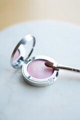 Pink blush compact with brush on a white marble surface for makeup application