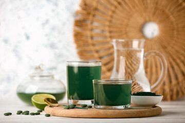 Glasses of fresh spirulina drink and pills on white wooden table, closeup