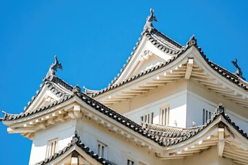 Fototapeta premium A traditional Japanese castle with white walls and black roofs, surrounded by a moat and trees.