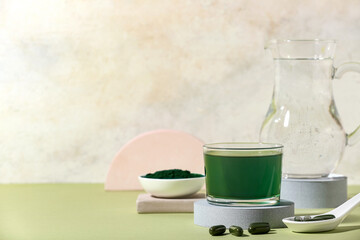 Glass of spirulina drink and pills on green table, closeup