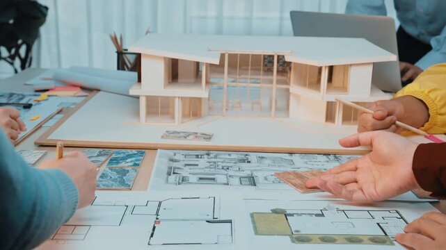 A vibrant workspace featuring hands of professionals engaged in collaborative architecture design, working on models, sketches, and blueprints in a modern office setting. SACTR