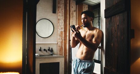 Mobile, brushing teeth and man in home for dental wellness, hygiene and morning news. Phone, cleaning mouth and shirtless person by bathroom doorway for oral care, health and reading message online