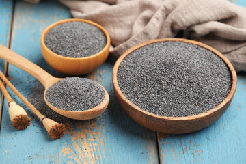 Bowls and spoon with poppy seeds on blue wooden background, closeup