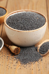 Bowl and scoop with poppy seeds on wooden background, closeup