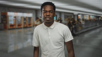 Young african american man wearing glasses and a white polo shirt walking through airport; confidence.