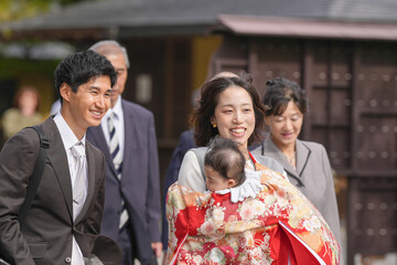A man and woman are smiling at a baby. The baby is being held by the woman. The man is wearing a suit and tie. The people are walking together