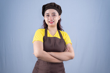 A smiling woman in a brown chef's hat and apron stands with crossed arms