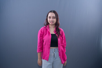 A smiling young woman in a pink shirt stands against a gray background