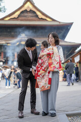 Fototapeta premium A man and a woman are standing in front of a building with a child in a red and white kimono
