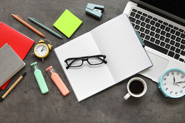 Alarm clock with laptop, cup of coffee, eyeglasses and office supplies on dark grunge background. Time management concept